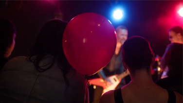 Red balloon floating in a crowded, low-lit bar with a band playing heavy metal music in the background